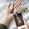 A hand holds a phone displaying a wooden NFC Bible necklace, showcasing its intricate design and functionality.