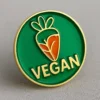 Green and orange enamel pin featuring the word "vegan," designed as a badge to promote veganism.