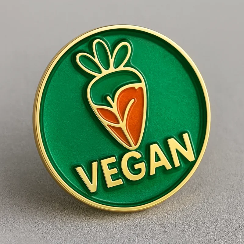 Green and orange enamel pin featuring the word "vegan," designed as a badge to promote veganism.