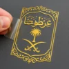 A person holds a paper displaying the Arabic word for Islam, with a metal phone sticker visible in the background.