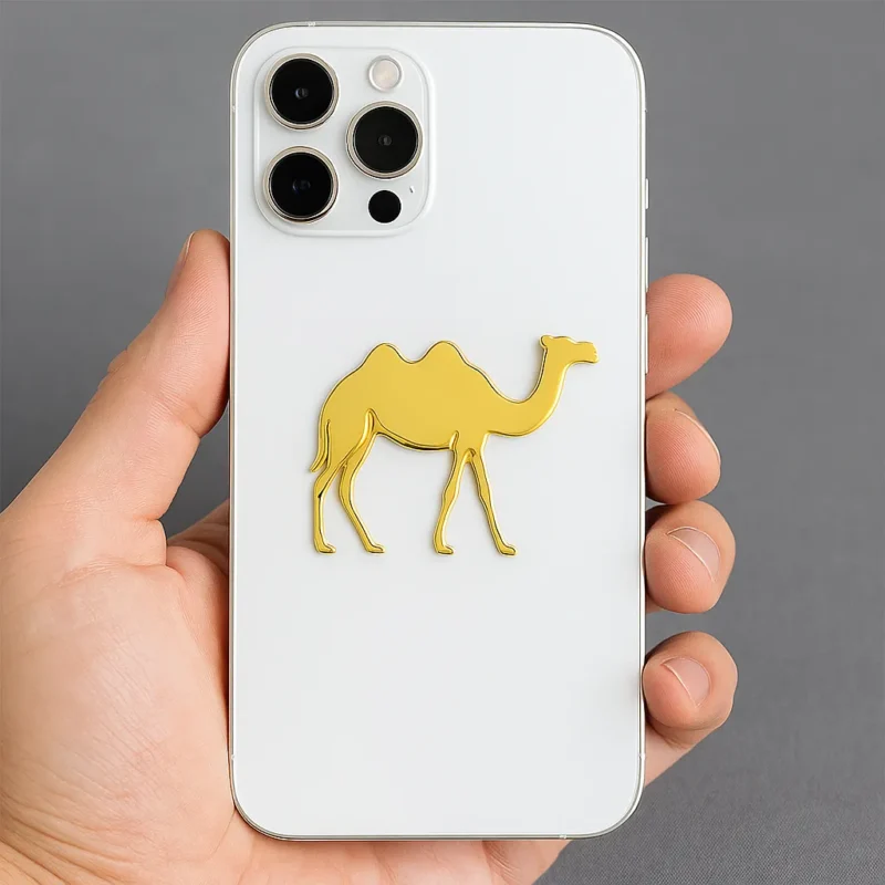Close-up of a person displaying a white iPhone case adorned with a gold camel metal sticker.
