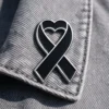 Black ribbon pin featuring a heart shape, symbolizing support and remembrance.