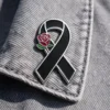 Black ribbon pin adorned with a red rose, symbolizing remembrance and tribute.