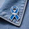 Blue awareness ribbon enamel pin with heart detail displayed on a denim jacket, representing support for health awareness and charity causes.