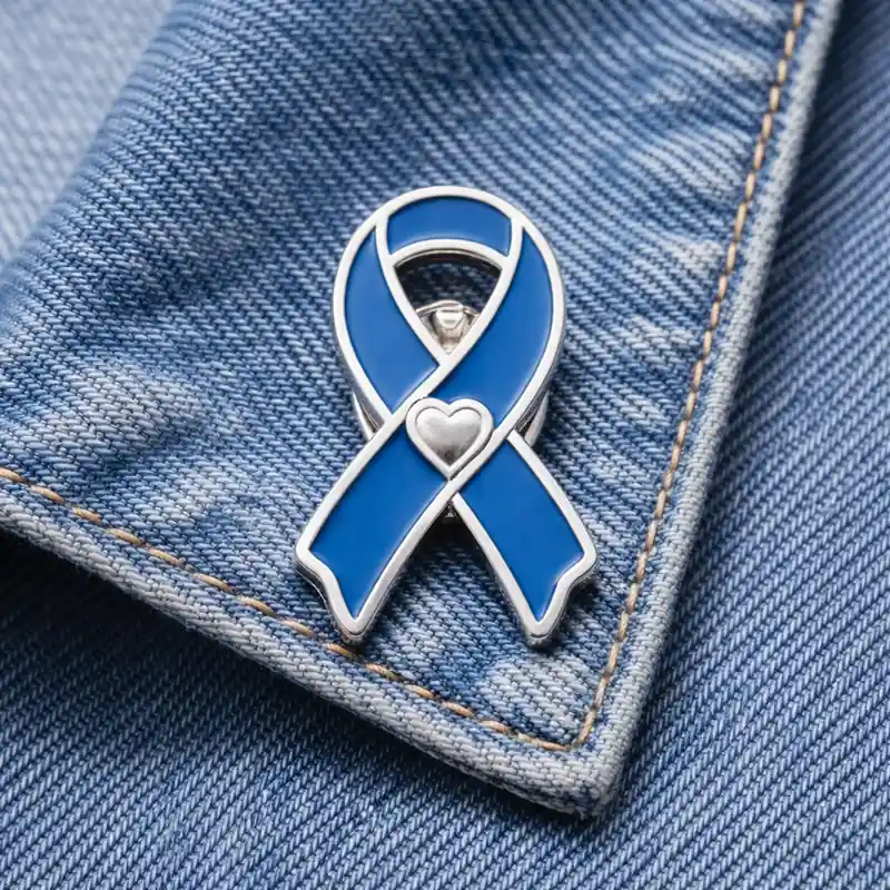 Blue awareness ribbon enamel pin with heart detail displayed on a denim jacket, representing support for health awareness and charity causes.