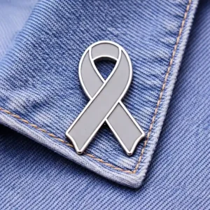A custom gray ribbon enamel pin displayed on a denim fabric background.