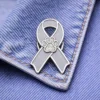 A custom gray ribbon enamel pin featuring a sparkling paw print design, displayed on denim fabric.