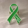 Close-up of a green awareness ribbon enamel pin with silver outline and custom text, symbolizing awareness and support for health and social causes.