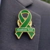 Green awareness ribbon enamel pin with gold outline and custom text, worn on a suit jacket to represent support for health awareness and social causes.