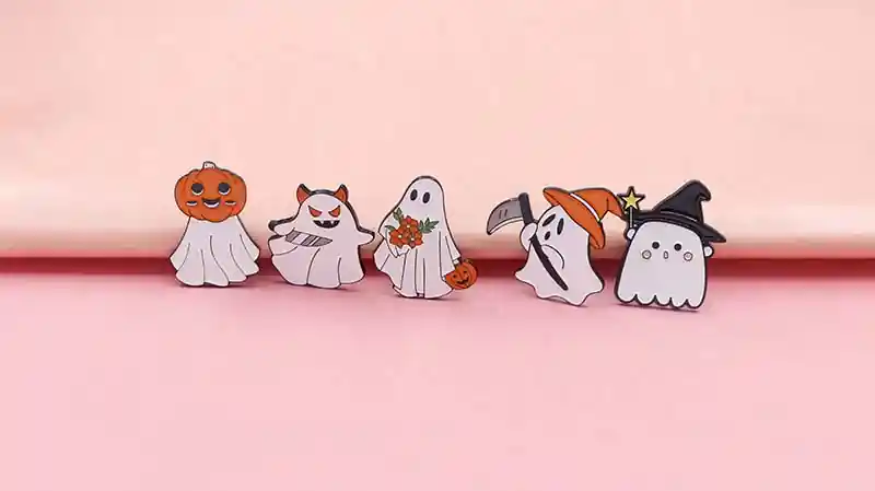 Set of cute Halloween-themed enamel pins featuring cartoon ghosts, pumpkin, witch hat, and spooky characters on a pink background