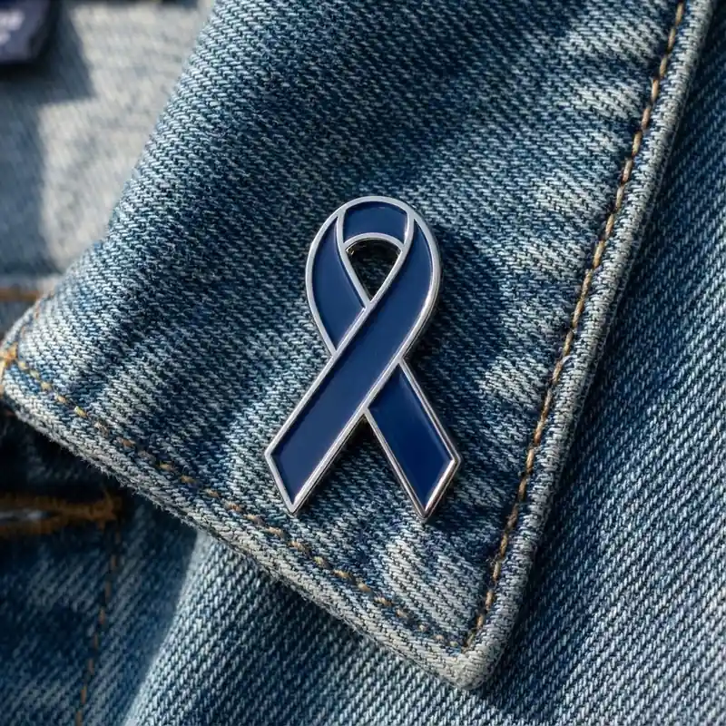 Dark blue awareness ribbon enamel pin displayed on a denim jacket, symbolizing support, awareness, and solidarity.