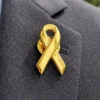 Gold awareness ribbon pin attached to a dark suit lapel, symbolizing childhood cancer awareness and support causes.