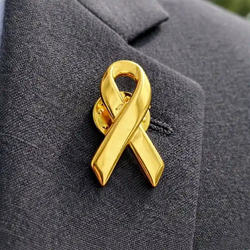 Gold awareness ribbon pin attached to a dark suit lapel, symbolizing childhood cancer awareness and support causes.