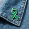 Green awareness ribbon enamel pin displayed on a blue denim jacket, symbolizing support for health awareness and charity causes.