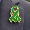 Green awareness ribbon enamel pin with gold outline and heart detail, worn on a suit jacket to symbolize support for health awareness and social causes.