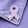 A lavender enamel ribbon pin with silver edges and a white daisy design attached to a denim jacket.