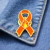 Orange awareness ribbon enamel pin with flame design, displayed on denim fabric, symbolizing support for fire-related causes or awareness campaigns.
