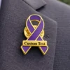 Purple awareness ribbon pin with gold trim and custom text plate, enamel lapel pin worn on a suit jacket for cancer awareness and social causes.