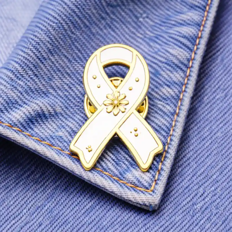 White awareness ribbon enamel pin with a floral design, displayed on denim fabric, representing support for general causes, charity events, or social initiatives.