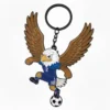 A cartoon eagle mascot wearing a blue soccer jersey with the number 2, kicking a soccer ball while flying with its wings spread, attached to a keychain.