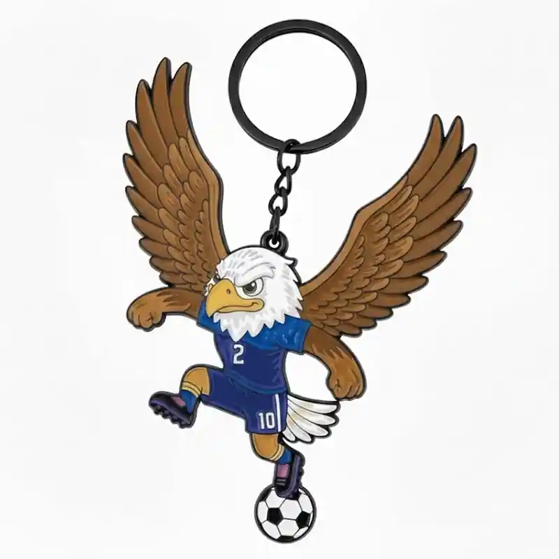 A cartoon eagle mascot wearing a blue soccer jersey with the number 2, kicking a soccer ball while flying with its wings spread, attached to a keychain.