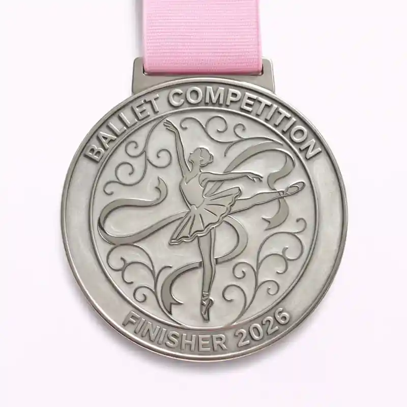 A silver ballet competition medal featuring a ballerina in a pose with flowing ribbons, surrounded by intricate swirling patterns. The inscription reads "BALLET COMPETITION" at the top and "FINISHER 2026" at the bottom.
