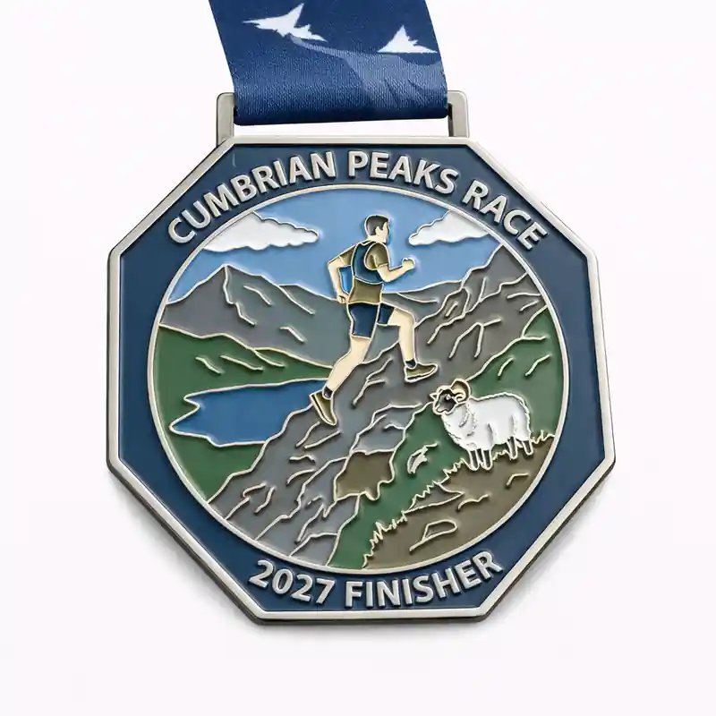 A silver and enamel medal for the Cumbrian Peaks Race, featuring a runner ascending a rocky mountain path with a lake and clouds in the background. A sheep is visible near the bottom. The medal has the text "CUMBRIAN PEAKS RACE" at the top and "2027 FINISHER" at the bottom. The ribbon is blue with a white mountain pattern.