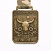 A bronze Desert Scorpion Challenge finisher medal featuring a desert scene with a cow skull, cacti, and rocky formations under a sun. Scorpions and snakes are positioned around the skull. The medal reads "DESERT SCORPION CHALLENGE" at the top and "2028 FINISHER" at the bottom.