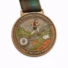 A bronze finisher medal for the Fell Running Championship featuring an image of a runner climbing a mountain, with a compass and a sheep in the foreground. The top of the medal reads "FELL RUNNING CHAMPIONSHIP," and the bottom says "FINISHER."
