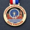A gold medal featuring the London Eye and Big Ben with the inscription "LONDON MARATHON 2024" and "2024 FINISHER" at the bottom, along with a red, white, and blue ribbon attached.