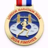 A gold medal with a design featuring Tower Bridge and a runner in motion, with the inscription "LONDON MARATHON 2024" and "2024 FINISHER" at the bottom, along with a red, white, and blue ribbon attached.
