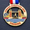 A gold medal featuring Tower Bridge and a runner in motion with the inscription "LONDON MARATHON 2024" and "FINISHER" at the bottom, along with a red, white, and blue ribbon attached.