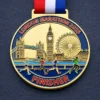 A gold medal featuring a design with runners in motion, Tower Bridge, Big Ben, and the London Eye, with the inscription "LONDON MARATHON 2025" and "FINISHER" at the bottom, along with a red, white, and blue ribbon attached.