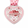 A heart-shaped silver medal featuring two hearts intertwined, with Cupid's arrows and the inscription "LOVE ON THE RUN 5K 2024 FINISHER" along with a pink ribbon decorated with heart patterns.