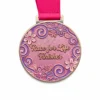 A round medal with a pink and purple floral design, featuring the words "Race for Life Finisher" in gold at the center. The medal is attached to a pink ribbon.