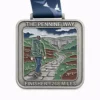 A silver medal for the Pennine Way 268 Miles featuring an image of a hiker walking along a stone path through a valley with cliffs in the distance. The scene includes rolling hills and dramatic skies. The medal is inscribed with "THE PENNINE WAY" and "FINISHER - 268 MILES," with a dark blue ribbon featuring a bird design.
