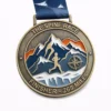 A bronze medal for "The Spine Race" 268 Miles featuring a mountain range with orange and blue accents. A runner is depicted in the foreground, with a compass symbol and snow-capped mountains in the background. The medal is inscribed with "THE SPINE RACE" and "FINISHER - 268 MILES" with a dark blue ribbon featuring bird motifs.