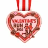 A heart-shaped rose gold medal featuring two runners, chocolates, and candy hearts with the inscription "VALENTINE'S RUN 2026" and a red and white ribbon attached.