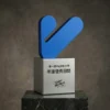 Trophée moderne bleu en forme de V monté sur une base cubique en métal brossé avec un texte chinois gravé, présenté sur une plate-forme en marbre foncé.