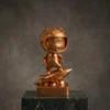 Figurine mascotte d'astronaute en bronze, debout sur une fusée, présentant un dessin animé futuriste et montée sur une base rectangulaire avec texte gravé.