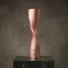 Trophée à colonne torsadée en cuivre avec un design en spirale lisse et un texte gravé, présenté sur une base en marbre foncé.