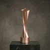 Trophée en cuivre torsadé en forme d'étoile, au design moderne et élégant, avec texte de base gravé, présenté sur une plateforme en marbre foncé.