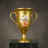 Coupe en or au design inspiré de Genshin Impact, ornée d'un emblème du personnage sur le devant, dotée de poignées décorées et posée sur un socle en marbre