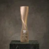 Trophée à colonne torsadée en or avec un design en spirale lisse et un texte gravé, présenté sur une base en marbre foncé.