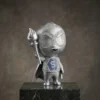 Figurine de mascotte de super-héros en argent tenant une torche, présentant des motifs gravés complexes et des ornements en cristal, présentée sur une base en marbre.