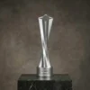 Trophée en forme d'étoile torsadée en argent, au design moderne et élégant, avec texte de base gravé, présenté sur une plate-forme en marbre foncé.