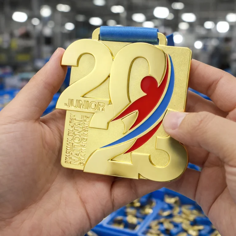ぼやけた工房の背景を背に、両手で「2023」と刻印された金色のメダルを掲げている。メダルには、様式化されたアスリートの姿とリボンがデザインされている。.