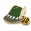 Spilla per cappello bavarese con piume alpine e contorni in metallo dorato in rilievo, cappello verde bosco, tesa grigia, fascia bianca blu e frizione a farfalla su sfondo bianco.