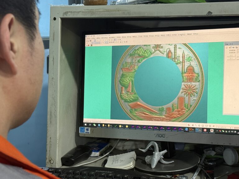 작업자가 컴퓨터 화면에 표시된 장식용 금속판의 상세한 3D CNC 조각 디자인을 면밀히 검사하여 제작 전 정확성을 확인하고 있습니다.