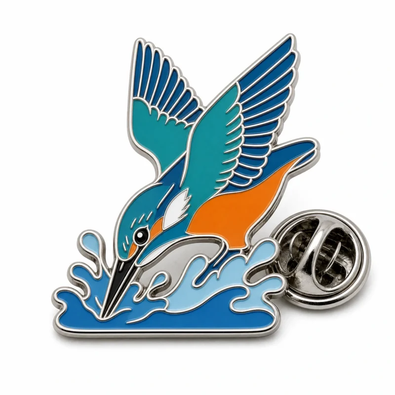 Épingle de martin-pêcheur plongeur avec contours en métal argenté poli, corps bleu sarcelle, ventre orange, gorge blanche, base bleue éclaboussée, et une pochette de papillon sur fond blanc.